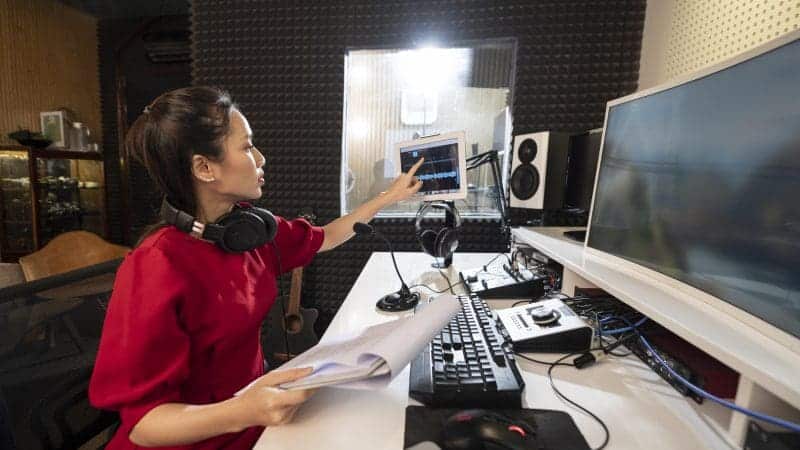 women in red dress looking at a pc screen and editing sound for a video.